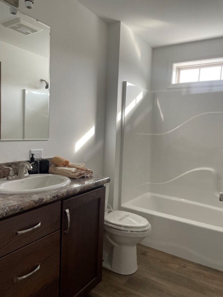 Bright bathroom with a white bathtub under a small window, brown vanity with a marble countertop, sink, and folded towels. Calm and tidy atmosphere.