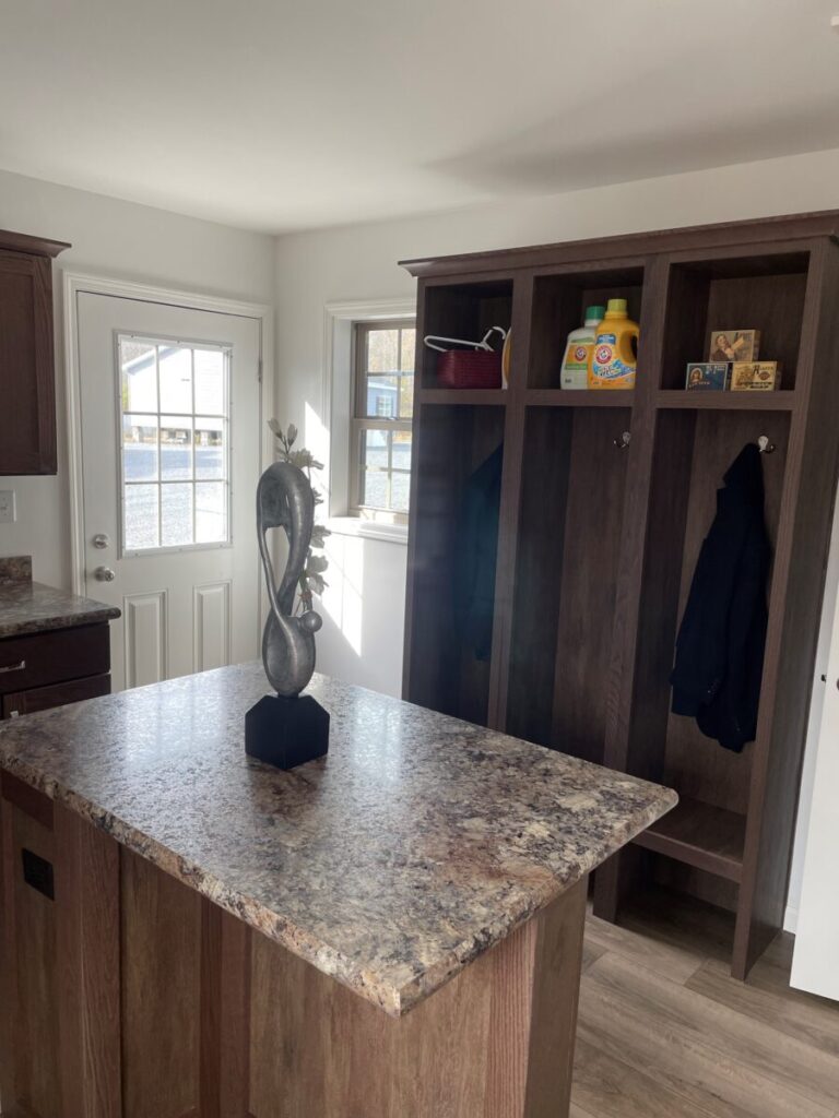 Cozy kitchen with dark wood cabinets, marble island, decorative sculpture, and warm sunlight through a window and door, creating a welcoming atmosphere.
