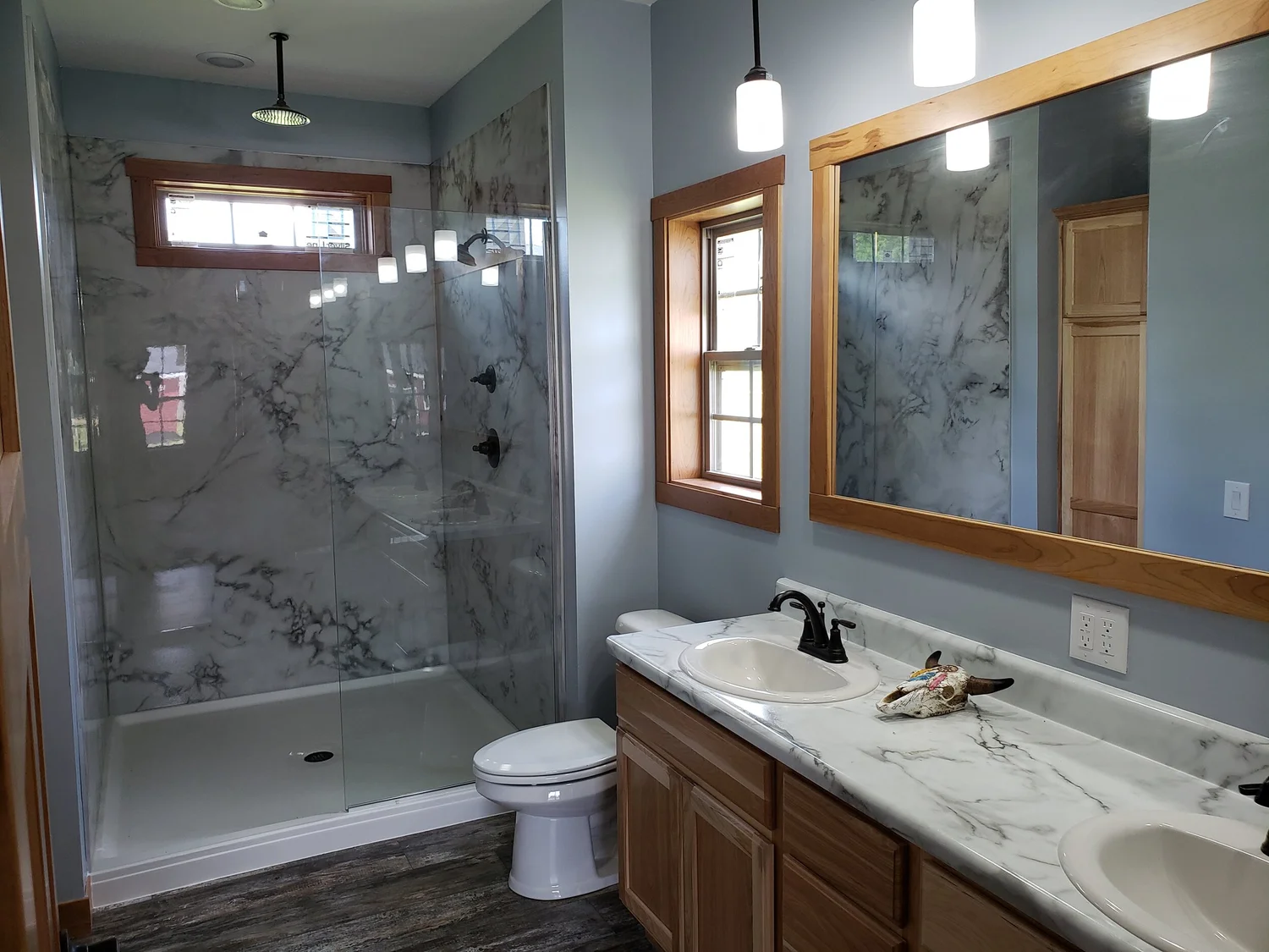 Modern bathroom with marble accents featuring a glass-enclosed shower, dual sinks with a marble countertop, wood cabinetry, and large mirrors.