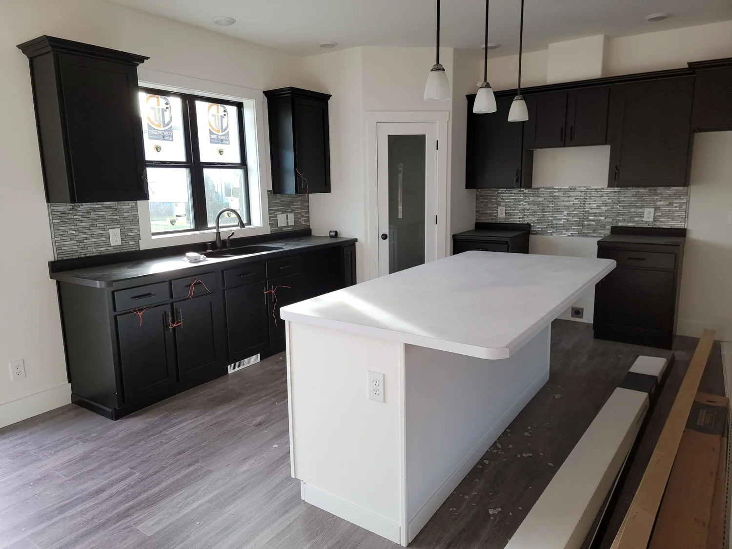 Modern kitchen with dark cabinetry, white countertops, and stainless steel fixtures. An island with pendant lights creates a sleek, contemporary look.