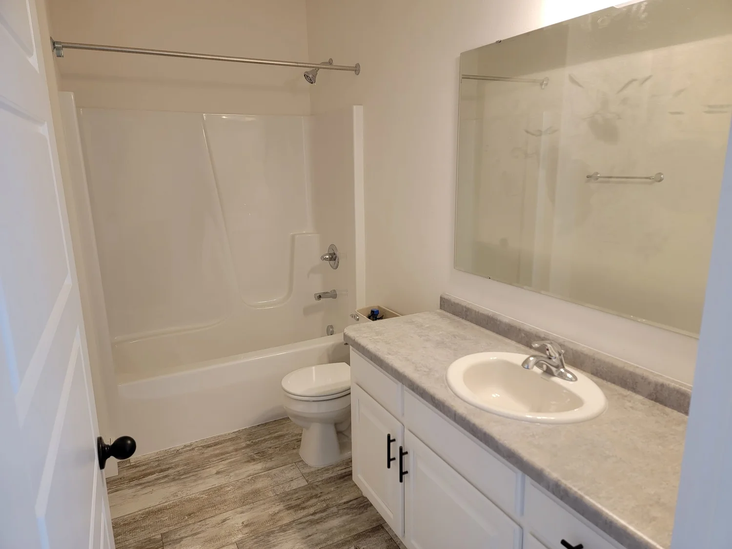 A modern bathroom with a white tub-shower combo on the left, a toilet in the center, and a vanity with a light gray countertop and sink on the right.