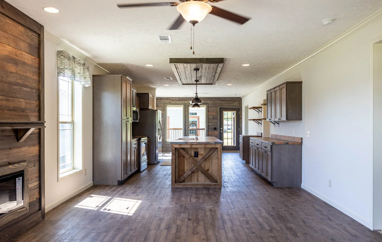 Spacious kitchen featuring rustic wooden cabinets, an island, and ceiling fan. Sunlight streams through large windows, creating a warm, inviting atmosphere.