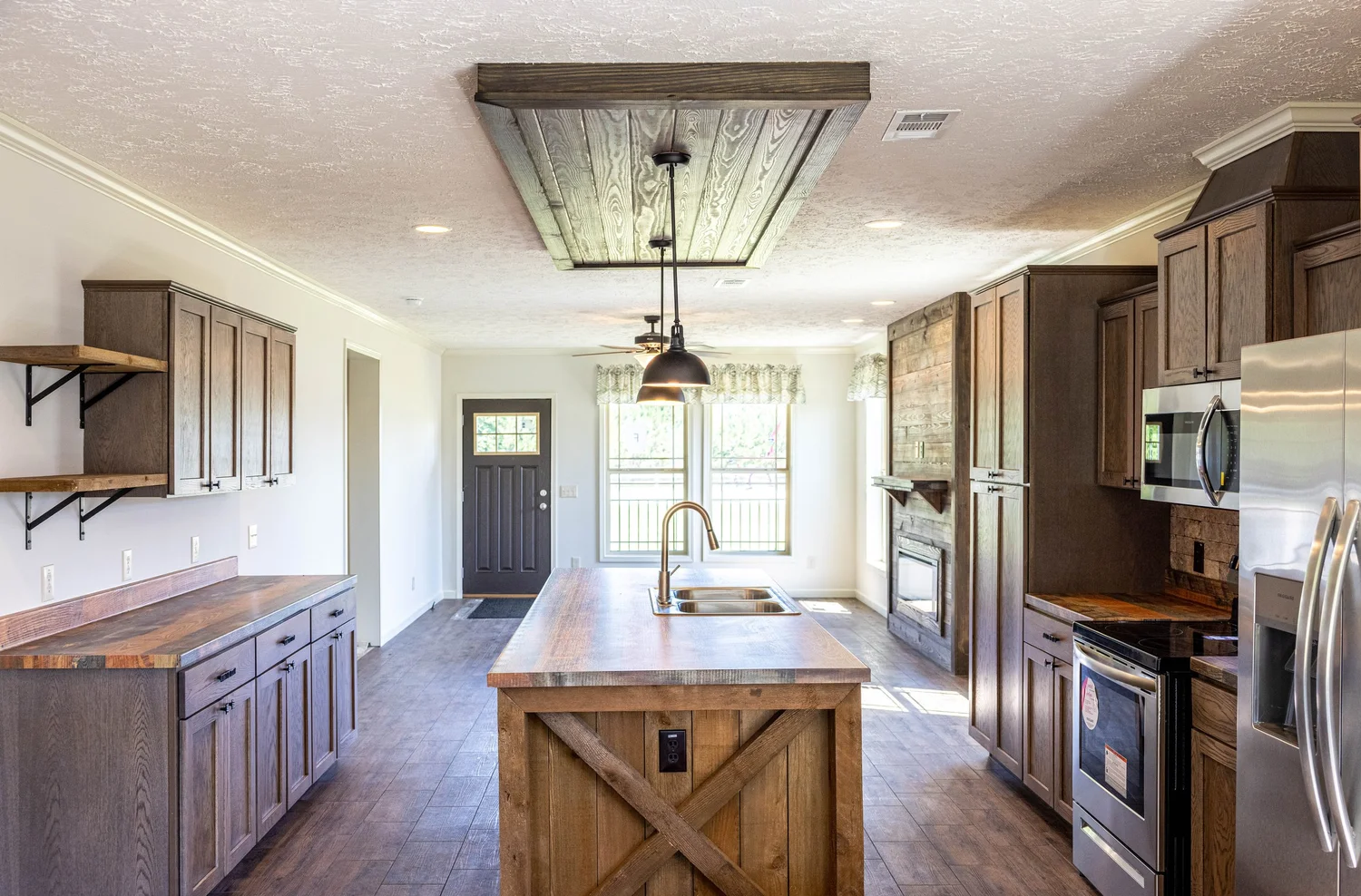 Rustic kitchen with wood accents, featuring an island with farmhouse sink, pendant lighting, stainless steel appliances, and large windows for natural light.