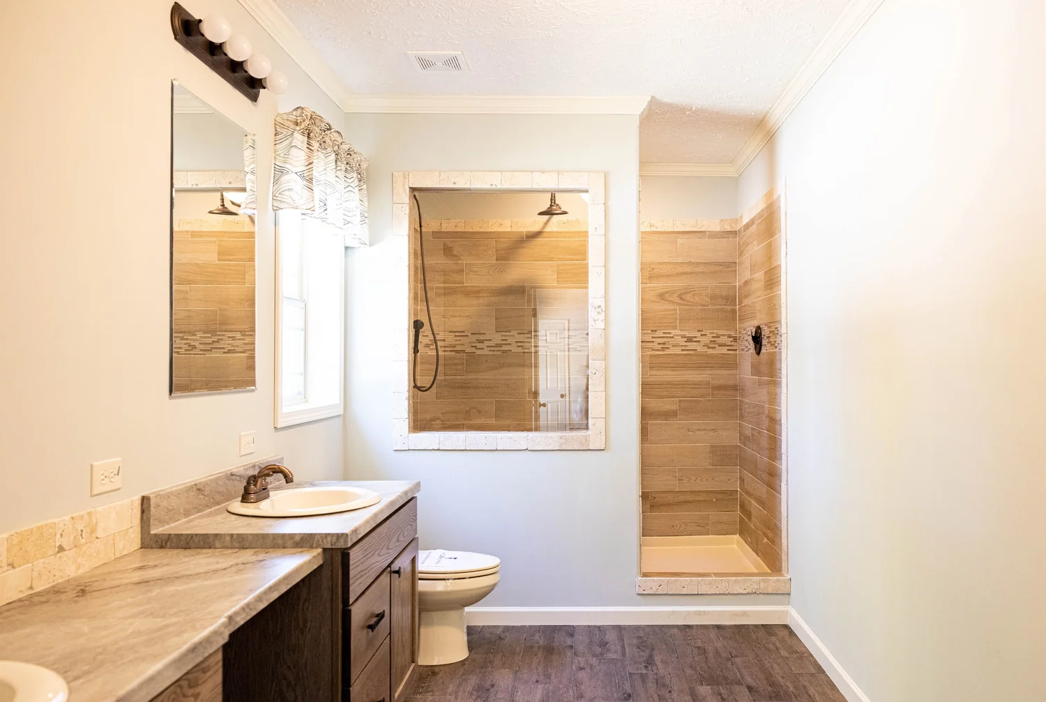 Modern bathroom with beige and wood accents. Features a glass-enclosed shower, wooden vanity with dual sinks, large mirrors, and natural light.