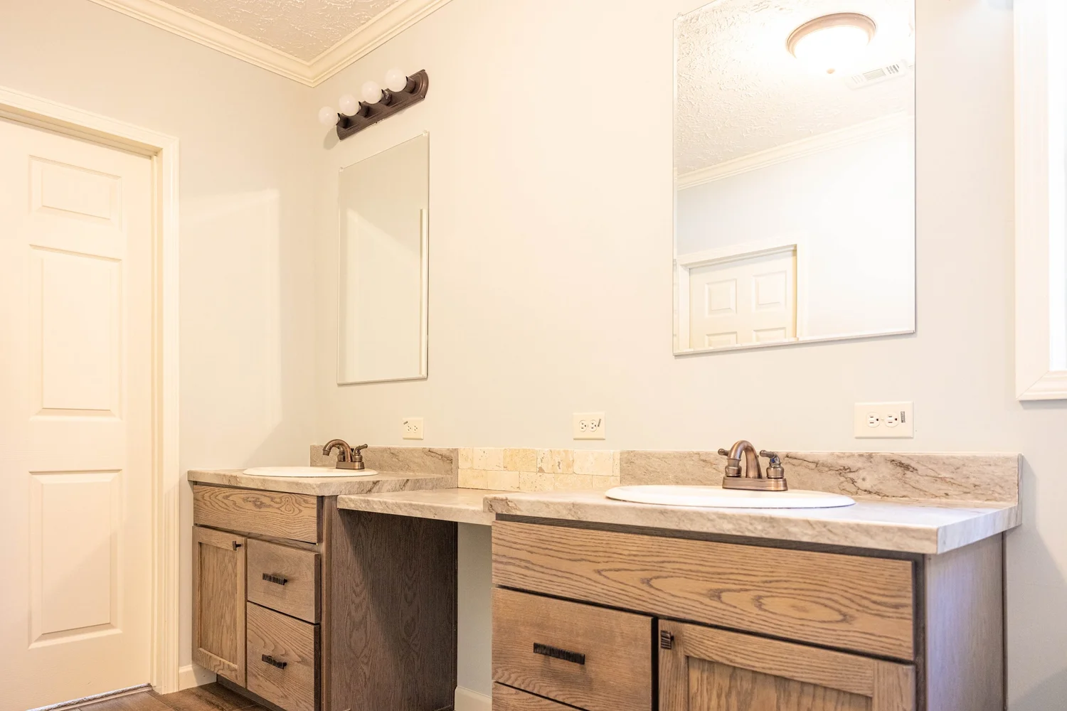 Modern bathroom with dual wooden vanities, marble countertops, and bronze fixtures. Two mirrors, soft lighting, beige walls, and minimalist design.