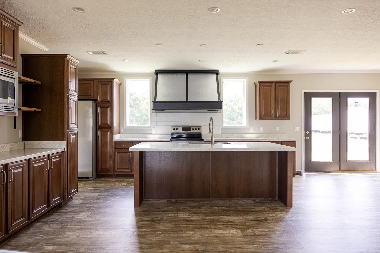 Spacious kitchen with wooden cabinets, a central island, stainless steel appliances, and abundant natural light from large windows and glass doors.