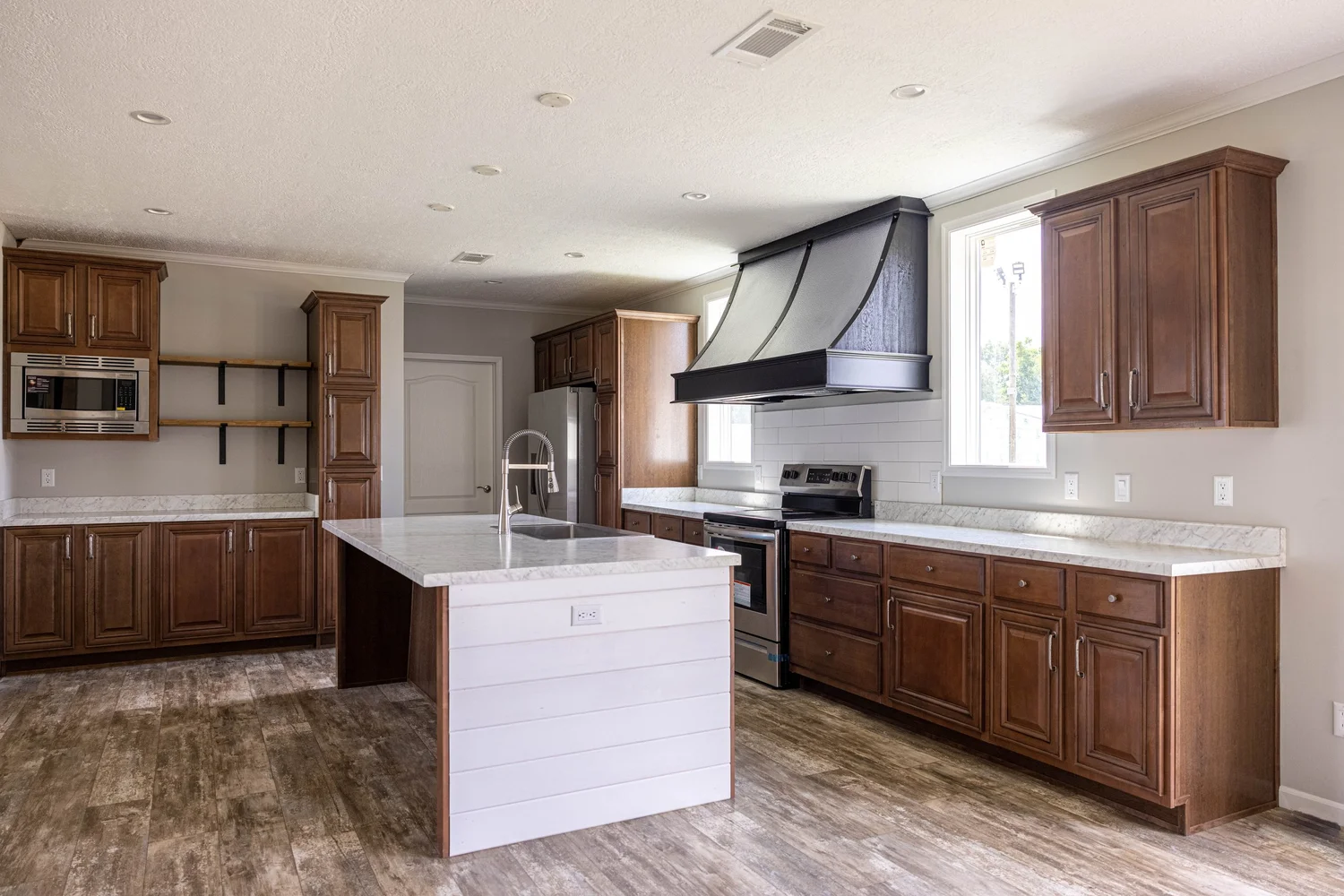 Spacious kitchen with wooden cabinets, modern stainless steel appliances, large island with marble countertop, and hardwood floors, conveying a sleek, cozy vibe.