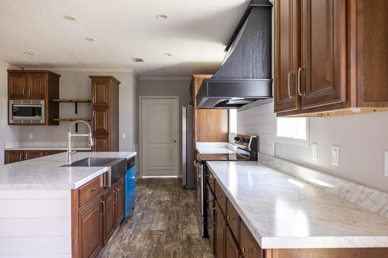 Spacious kitchen with wooden cabinets, marble countertops, and stainless steel appliances. Bright natural light and a warm, inviting ambiance.