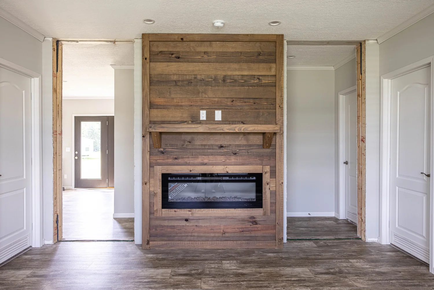 Rustic room with a wooden accent wall featuring an inset fireplace. Flanked by white doors and open doorways, the space feels warm and inviting.