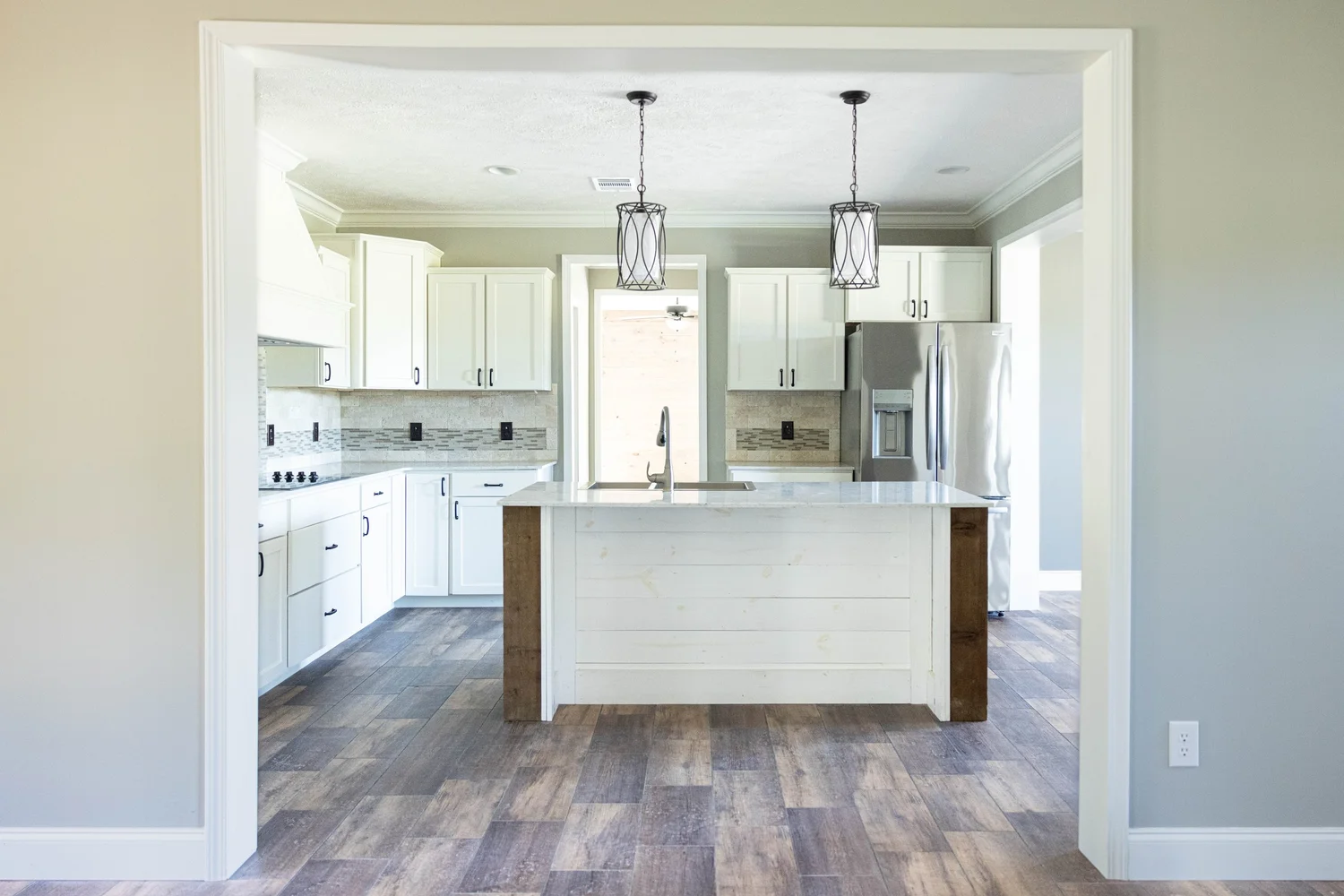 Modern kitchen with white cabinets, a central island with wood accents, pendant lights, and stainless steel appliances. The space feels bright and open.