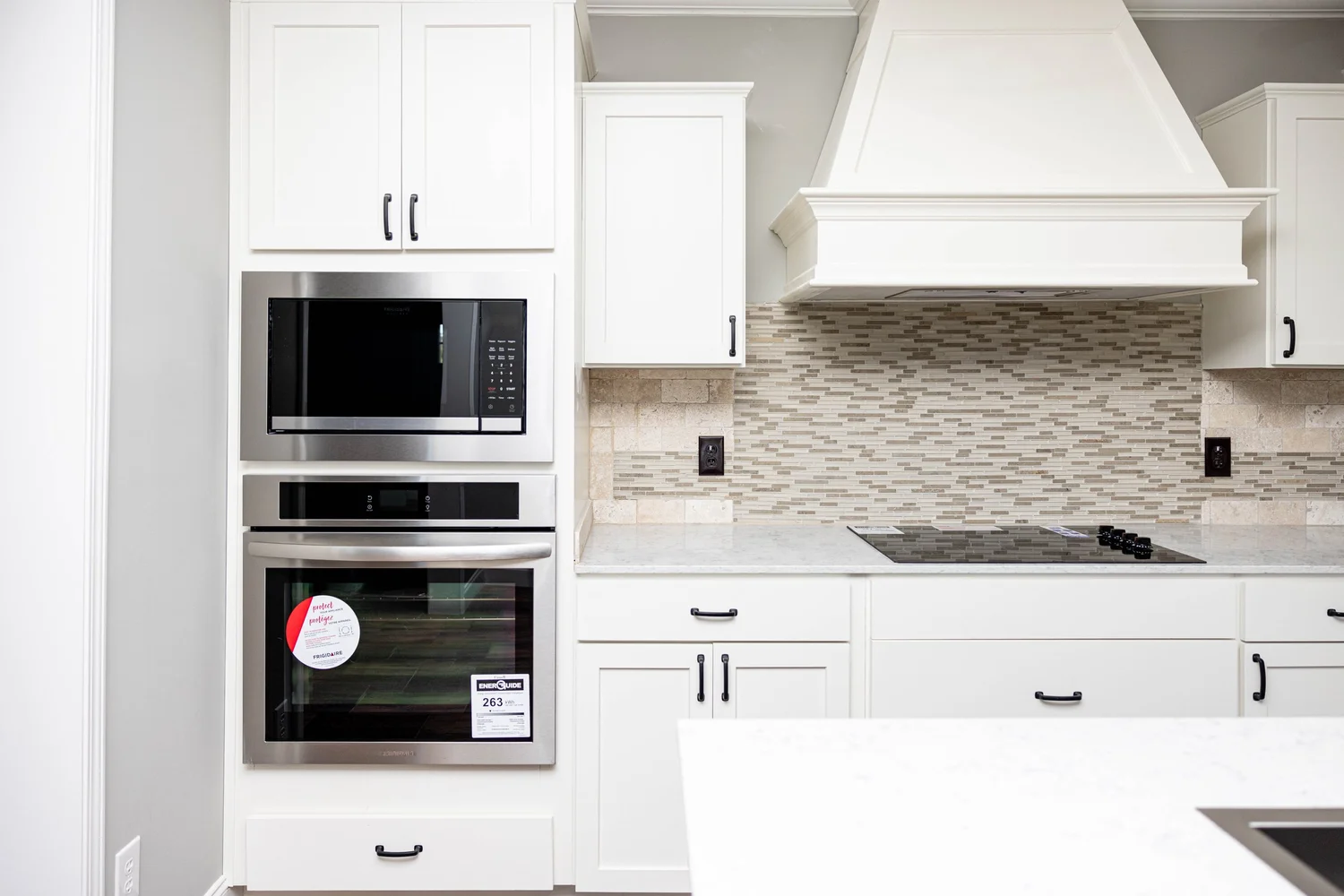Sleek kitchen with white cabinets and a modern stainless steel oven and microwave. A mosaic tile backsplash adds texture above the smooth countertop.