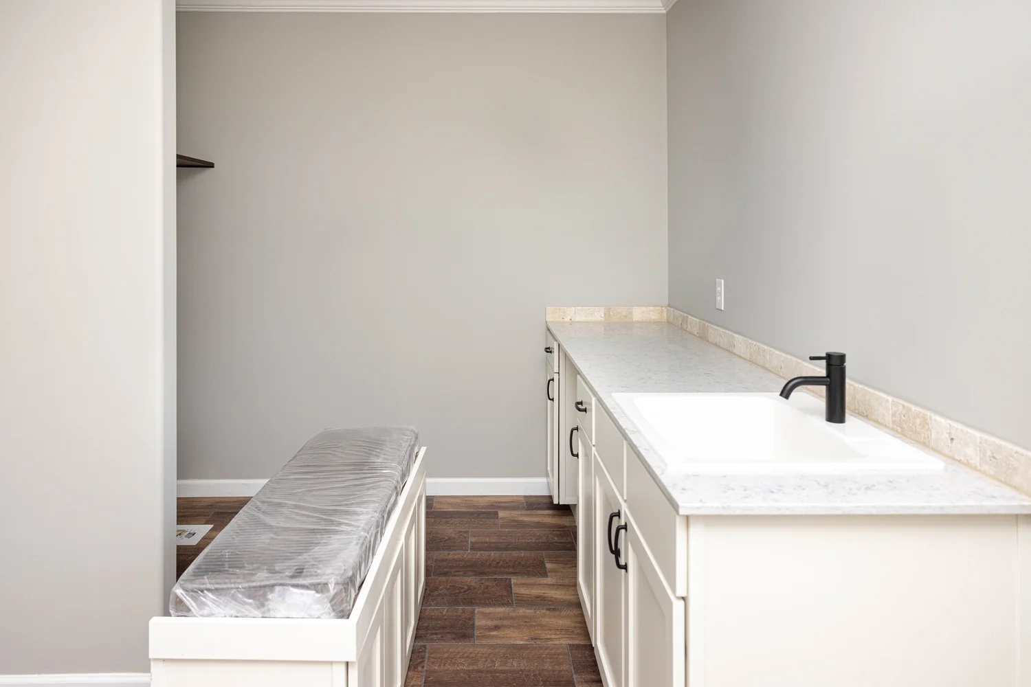 Minimalist laundry room with beige walls featuring a white countertop and sink, black faucet, light cupboards, and dark wood flooring. Modern and clean.
