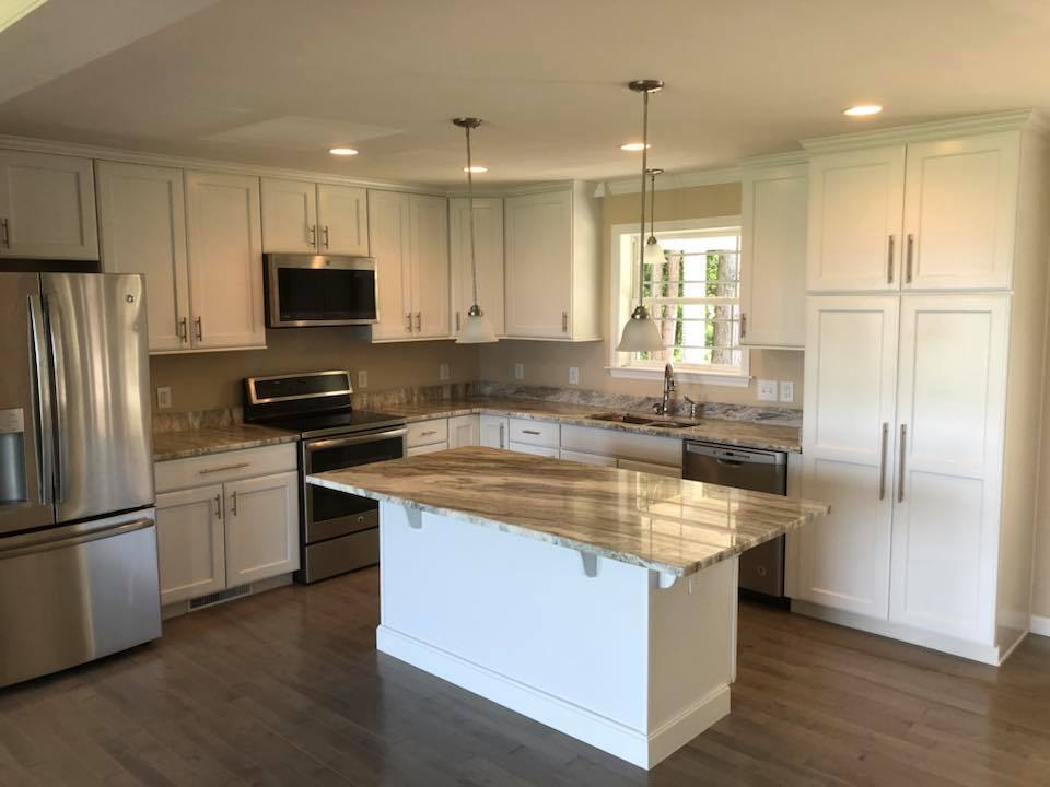 Modern kitchen with white cabinets, stainless steel appliances, and a central island. Pendant lights hang above the granite countertop, creating a bright, inviting space.