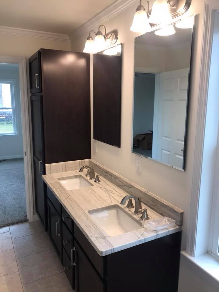 Elegant bathroom with a double vanity sink. Features dark wood cabinets, marble countertop, dual mirrors, and soft overhead lighting, creating a fresh, inviting ambiance.