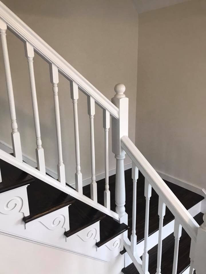 White-painted staircase with dark wood steps and detailed balusters, creating a classic and elegant appearance. Soft lighting highlights the design.