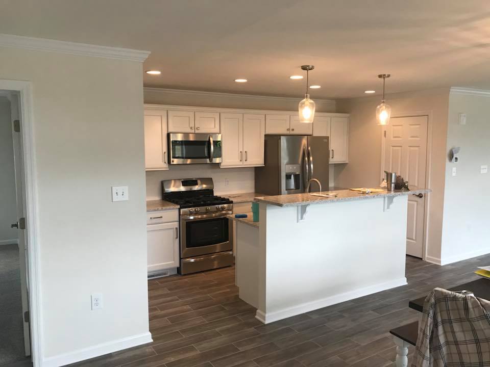 Modern kitchen with a warm ambiance, featuring white cabinets, stainless steel appliances, granite countertops, pendant lighting, and wood-look tile flooring.