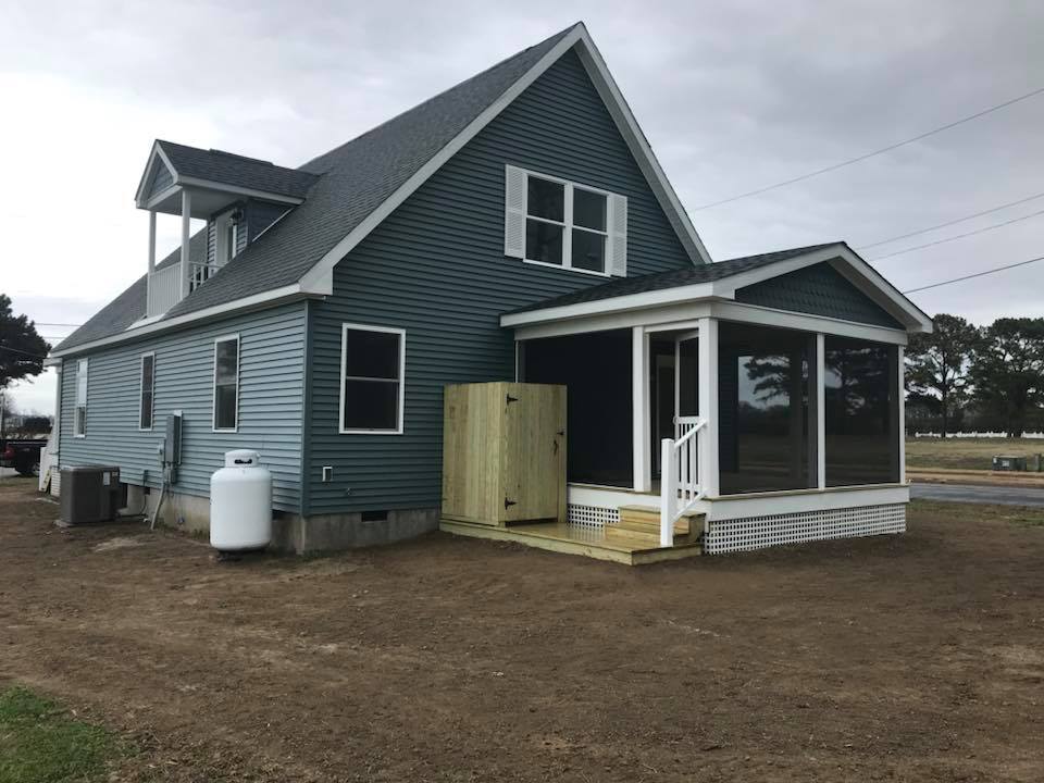 Gray two-story house with blue siding and white trim, featuring a screened porch and small wooden deck. Overcast sky with a rural setting.