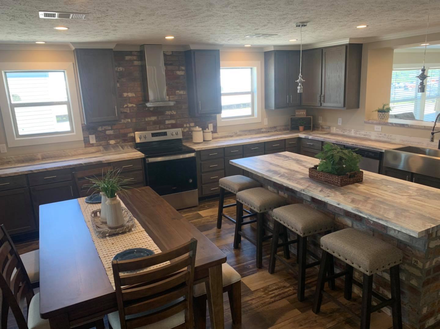 A cozy kitchen with dark wood cabinets, a stone backsplash, and a central island with stools. Warm lighting and a wooden dining table add a welcoming feel.