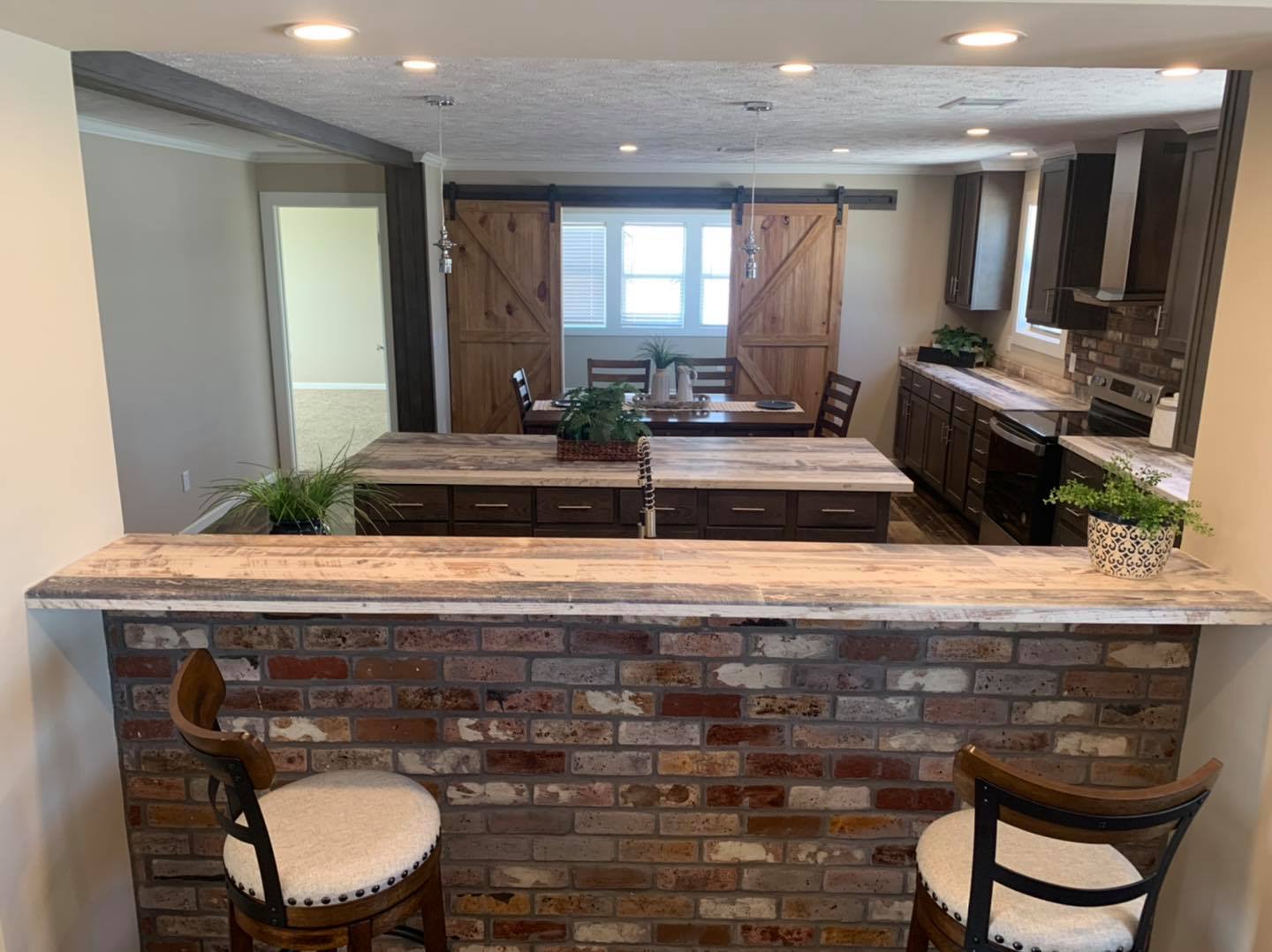 Cozy kitchen-dining area with rustic brick bar counter, wooden cabinetry, barn-style sliding doors, and warm lighting. Plants add a fresh touch.