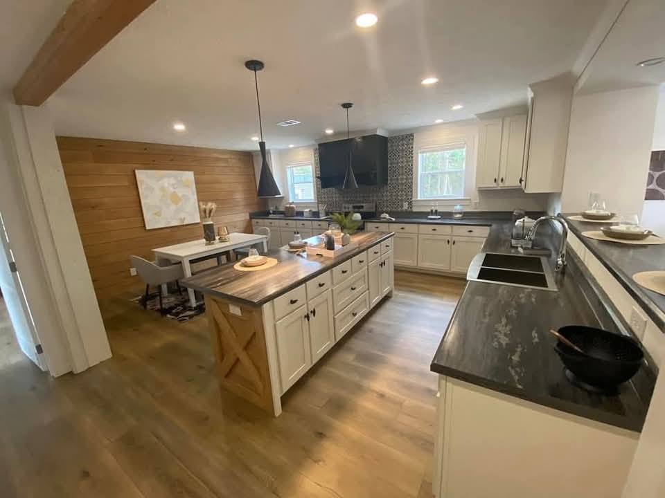 Spacious modern kitchen with white cabinets, dark countertops, and wooden flooring. Central island with seating area. Bright, inviting atmosphere.