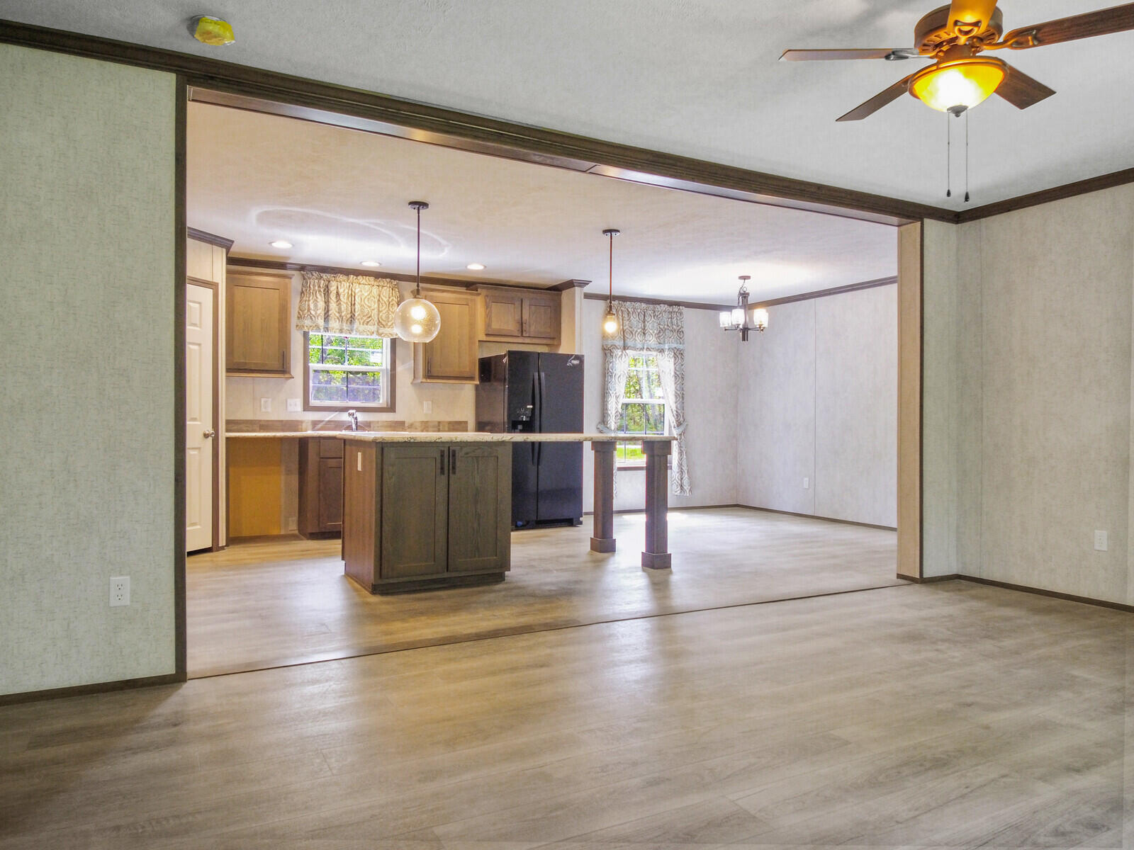 Open-concept kitchen with light wood flooring, dark cabinetry, and modern pendant lighting. Adjacent dining area with a window and ceiling fan.
