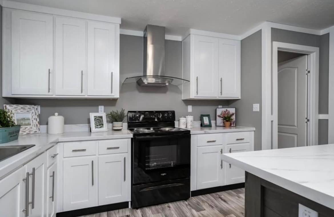 Modern kitchen with white cabinets, gray walls, and light wood flooring. Features a sleek black oven, stainless steel hood, and marble countertop.