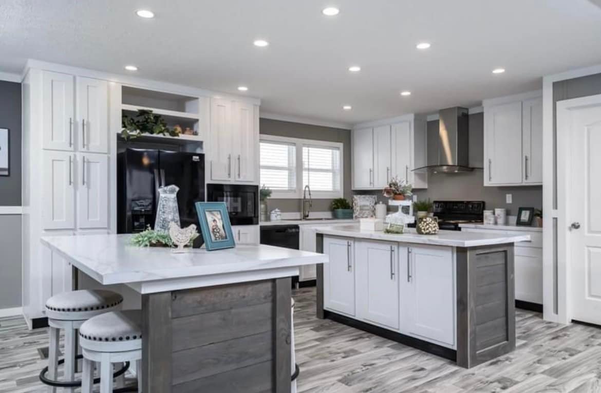 Modern kitchen with white cabinetry, gray accents, and a central island featuring bar stools. Bright lighting and decor create an inviting atmosphere.
