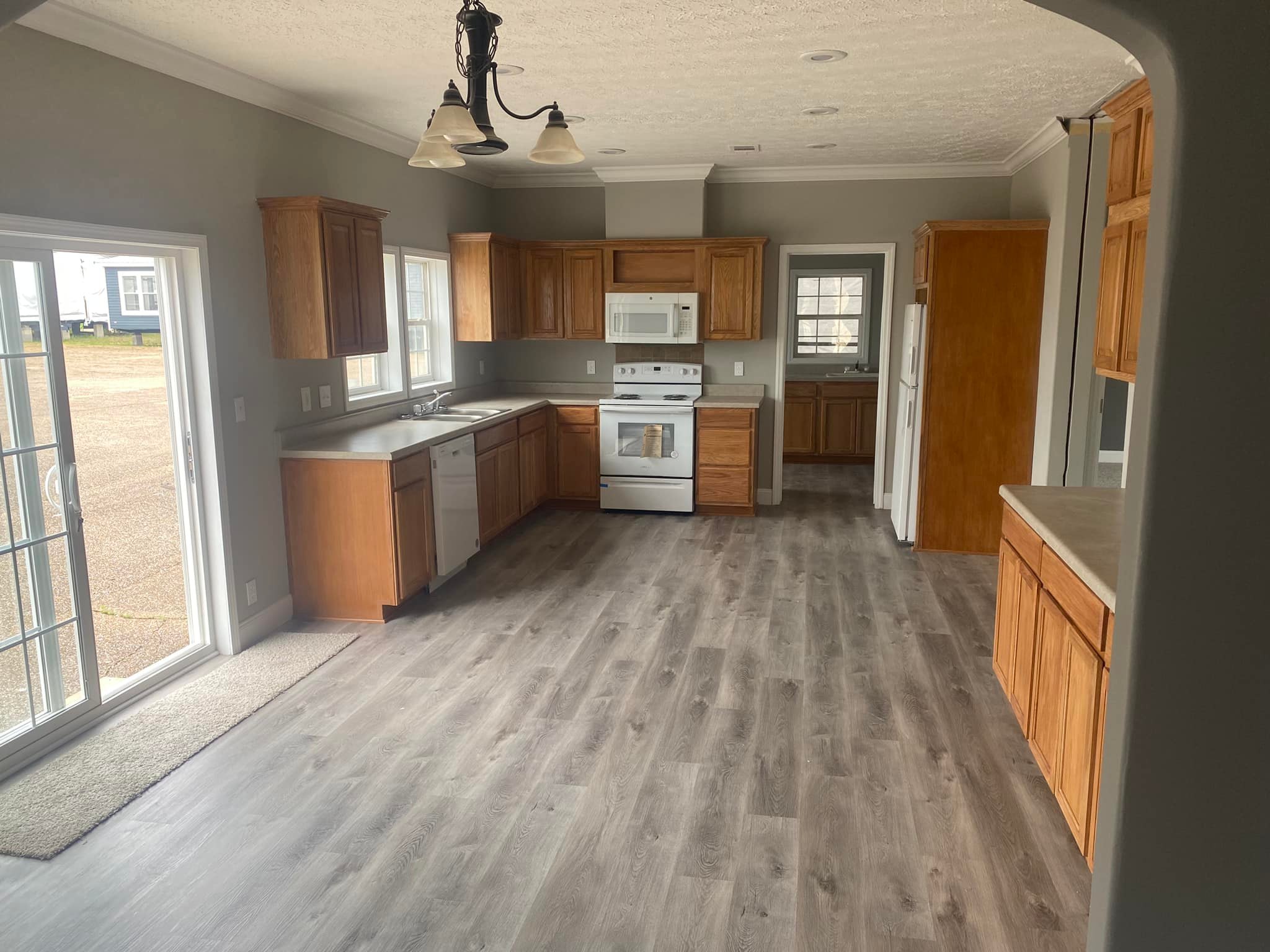 Spacious kitchen with light hardwood floor, wooden cabinets, and modern appliances. Sunlight streams through large patio doors, creating a warm, inviting atmosphere.