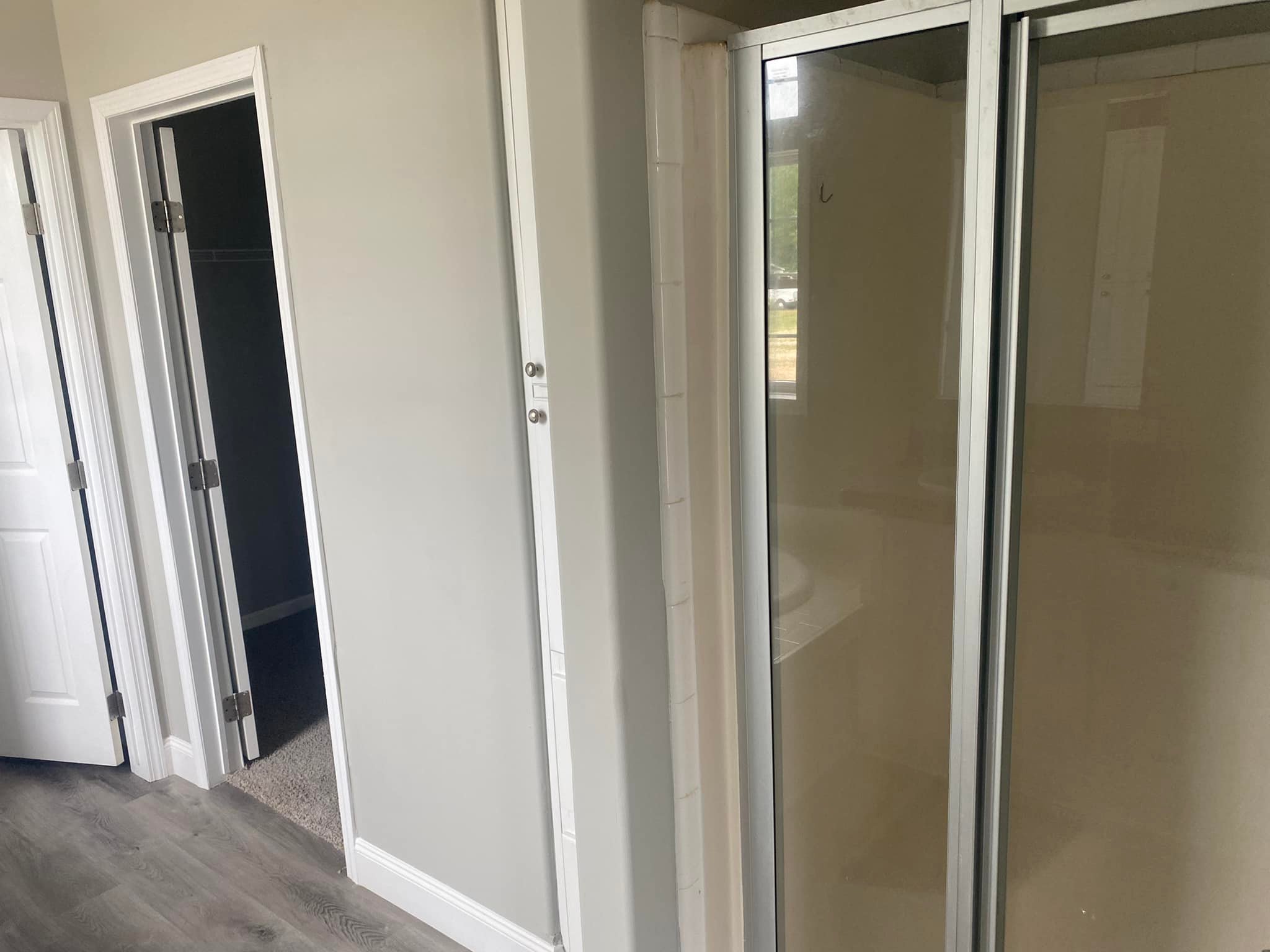 A modern bathroom features a glass shower enclosure with sliding doors. Adjacent is a small hallway with doorways leading to a closet and another room. Bright and clean ambiance.