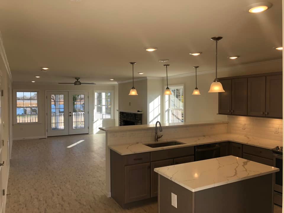 Spacious open-plan kitchen and living room with marble countertops, pendant lights, and large windows. Bright natural light, inviting and modern ambiance.