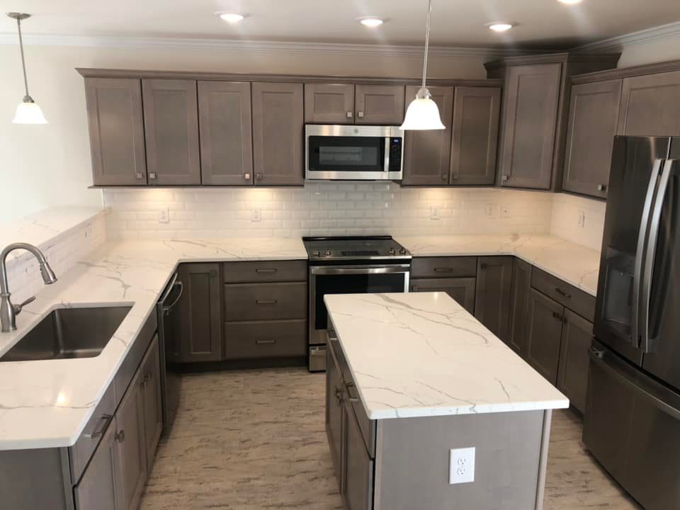 Modern kitchen with gray cabinets, marble countertops, and a white tile backsplash. Stainless steel appliances and pendant lighting add elegance.
