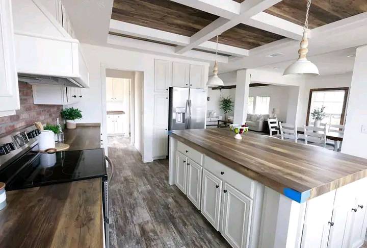 Spacious, modern kitchen with wooden floors and a coffered ceiling. Features a large island, stainless steel appliances, and pendant lighting.