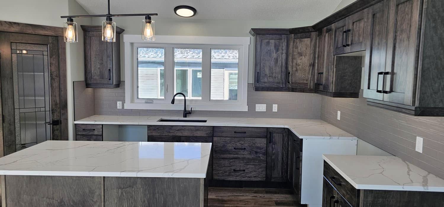 Modern kitchen with dark wood cabinets, white marble countertops, and an island. Three pendant lights hang above. A window offers natural light.