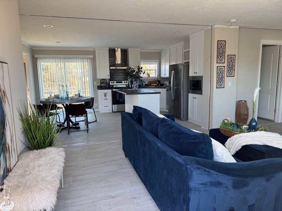 Open-concept living room and kitchen with a navy blue sofa, fur-covered bench, and dining table. Bright, modern, and welcoming ambiance.