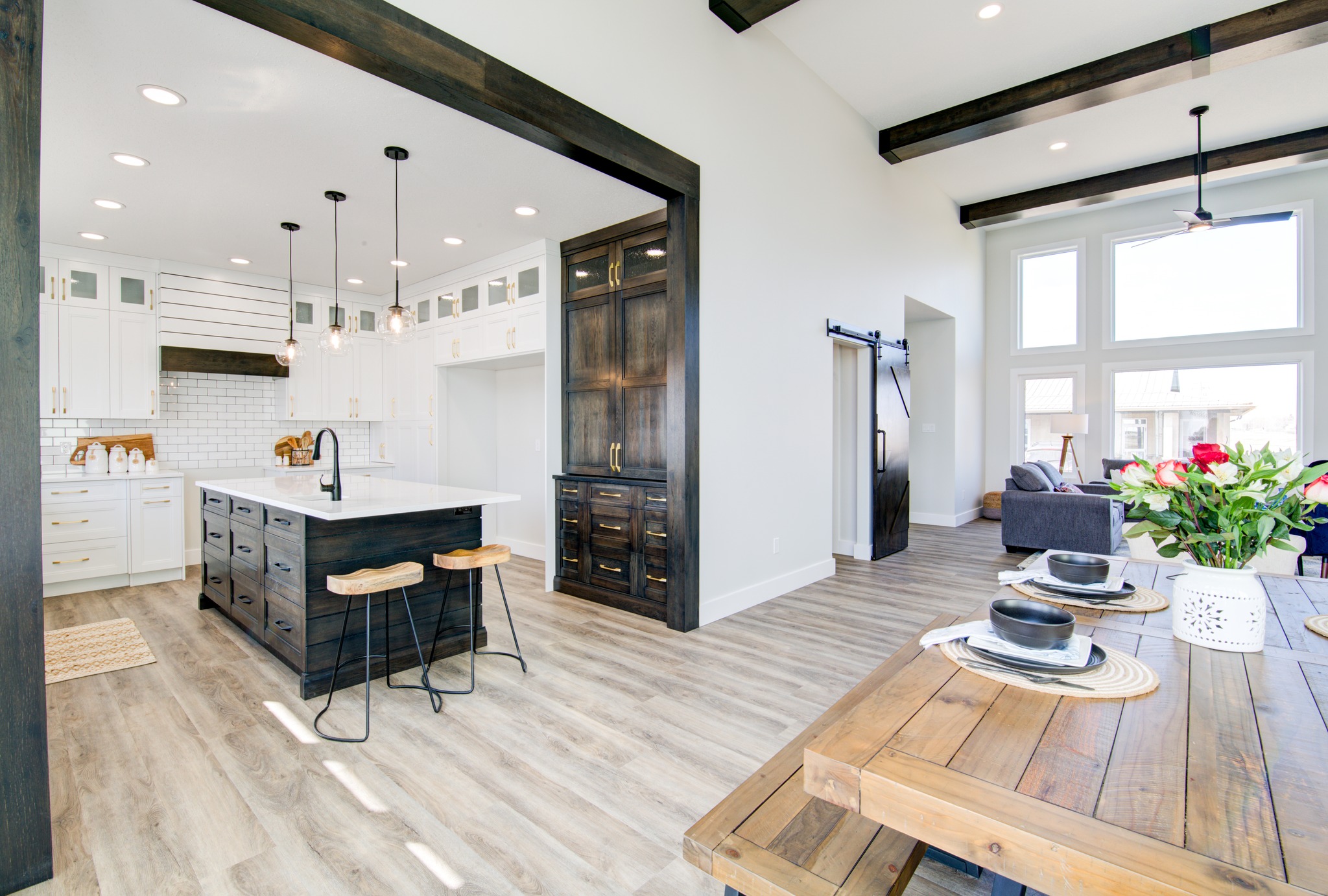 Spacious modern kitchen with white cabinets, black island, and wooden accents. Nearby dining area and large windows create a bright, welcoming space.