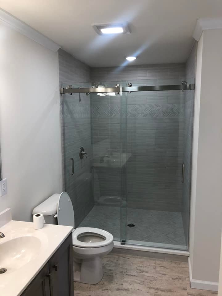 Modern bathroom with a glass shower enclosure featuring sliding doors, a white toilet, and a sink with a countertop. Neutral tones create a clean, serene atmosphere.