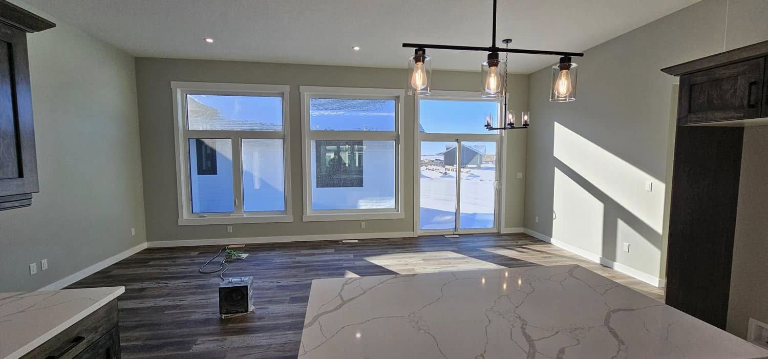 Modern living room with large windows showcasing a snowy landscape. Sunlight streams in, illuminating marble countertops and wooden flooring, creating a warm, inviting ambiance.