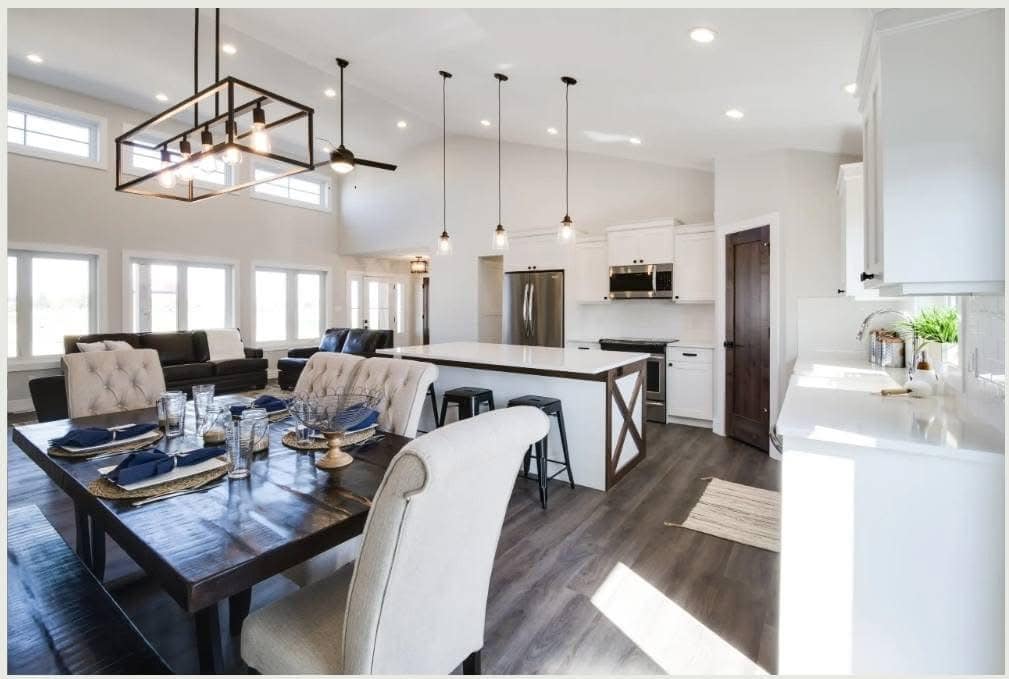Spacious modern kitchen and dining area with high ceilings, white cabinetry, and dark wood flooring. A large table is set with blue accents, creating an inviting atmosphere.