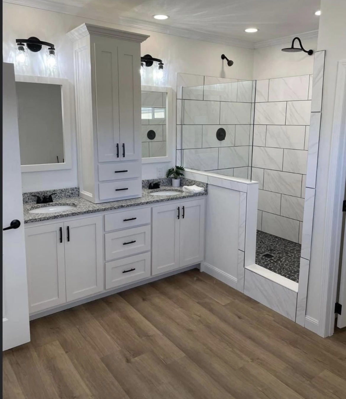 A modern bathroom features a double sink vanity with white cabinets and gray granite countertop. A glass shower with tiled walls and wooden floor add elegance.