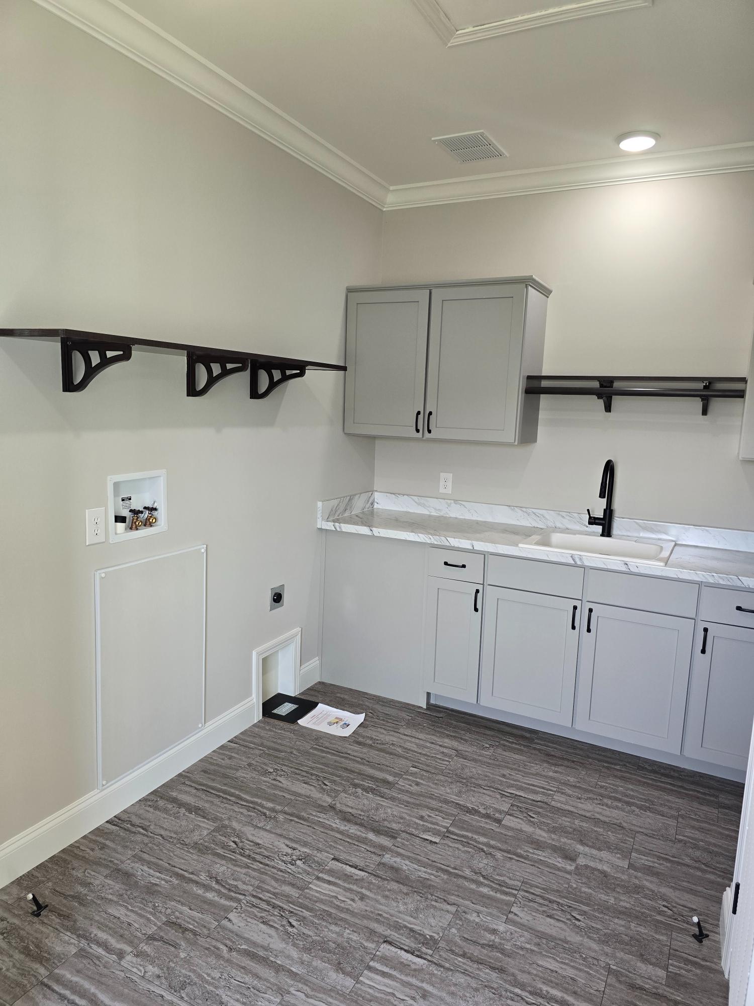 A modern laundry room with gray cabinets, marble countertop, and black faucet. Open shelves and tile flooring create a clean, minimalist look.