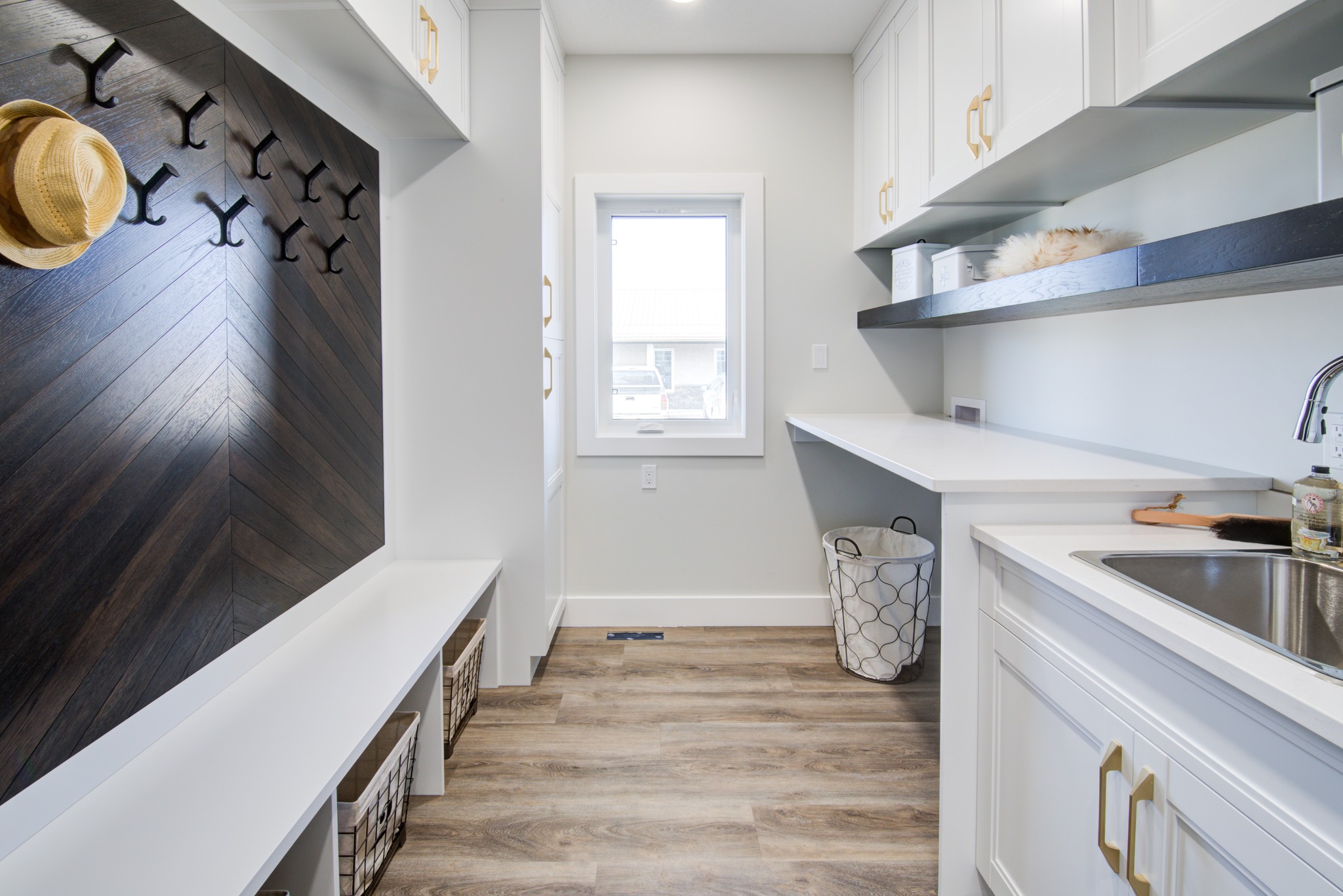 Bright and modern mudroom with white cabinets, wooden floor, and coat hooks. A straw hat hangs on the wall. Calm, organized atmosphere.