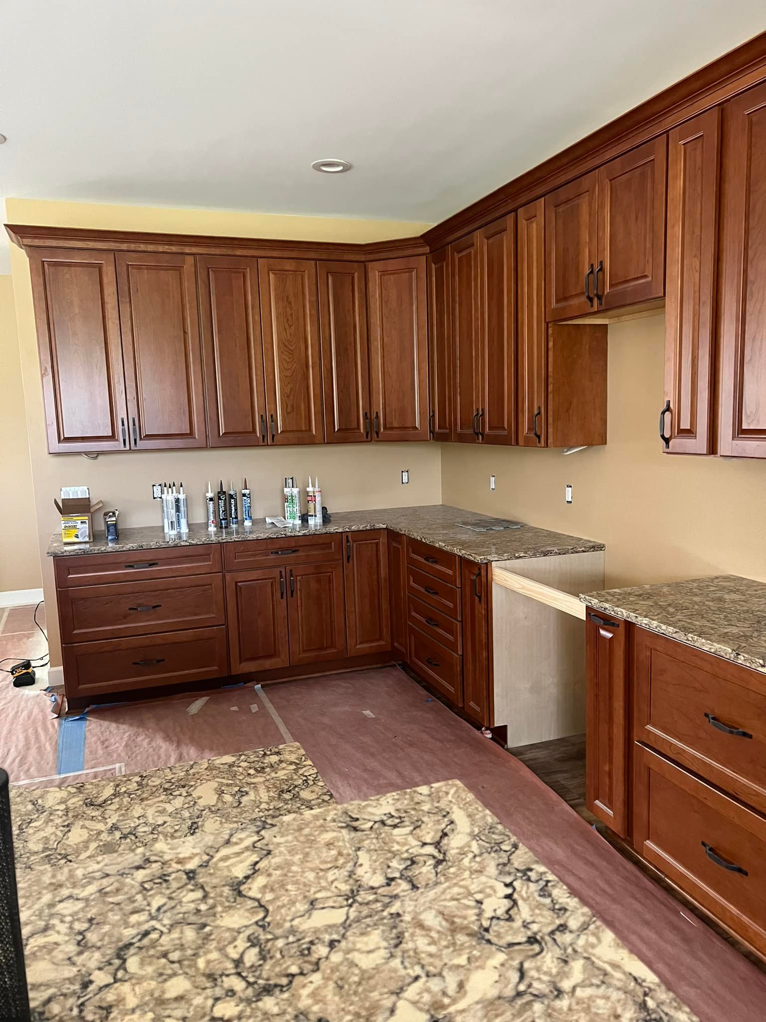 Warm, inviting kitchen with rich brown wooden cabinets and granite countertops. Supplies on counter hint at ongoing renovations, creating a sense of progress.