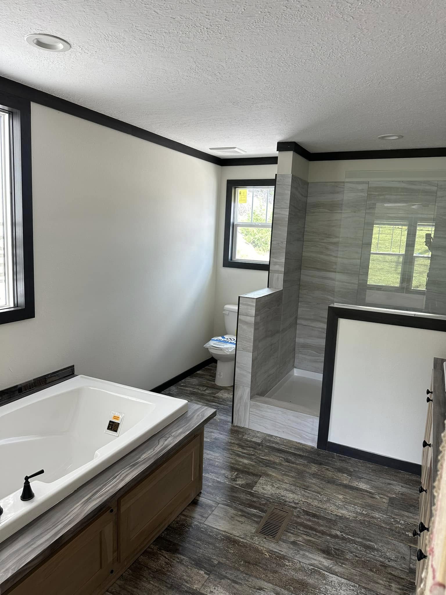 Modern bathroom with a large bathtub, wood accents, and a sleek, open shower. Natural light streams through a window, creating a serene atmosphere.
