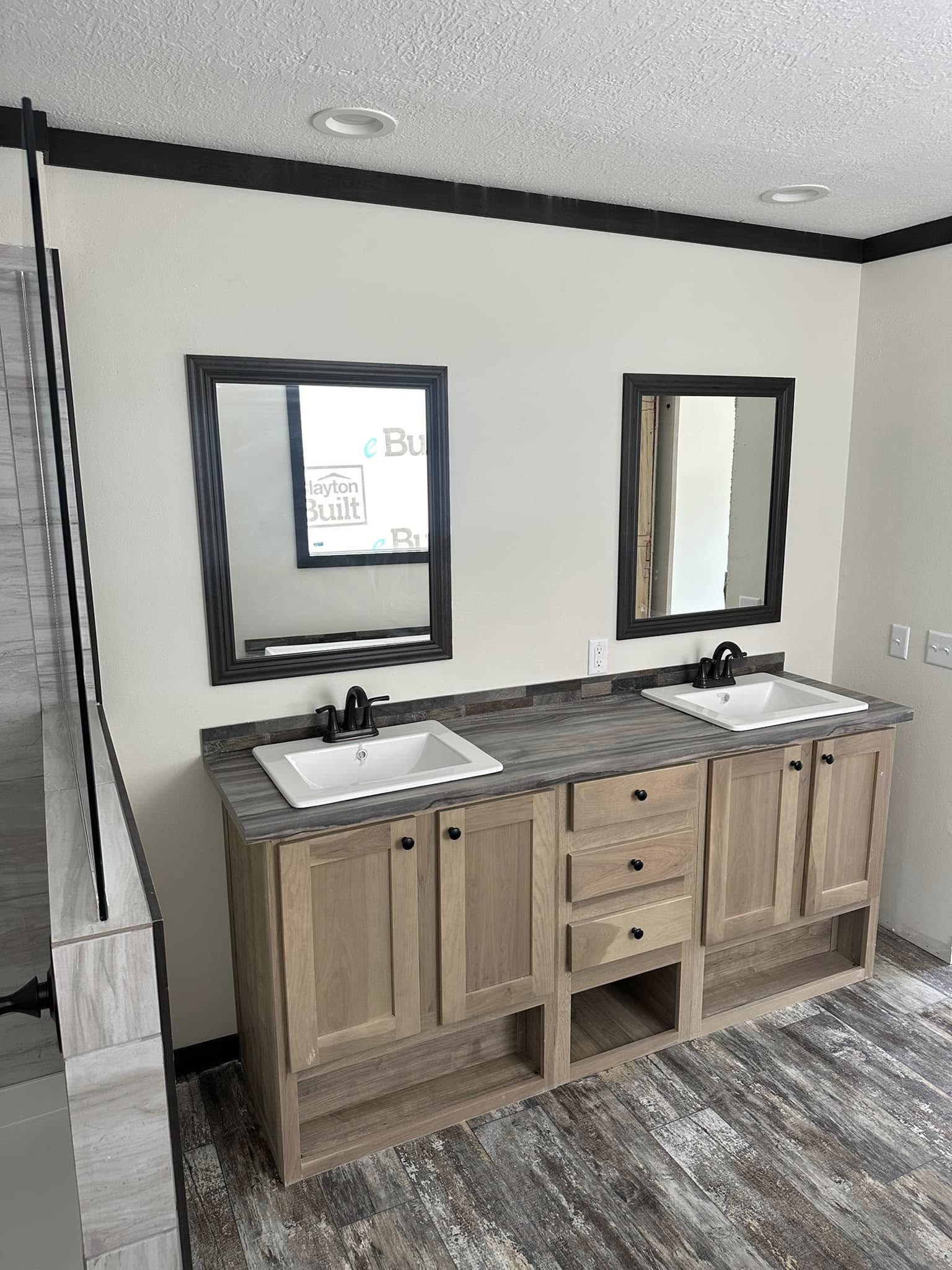 Rustic bathroom with a wood vanity, two rectangular sinks, black faucets, and two mirrors. The floor is wooden, emitting a cozy, serene vibe.