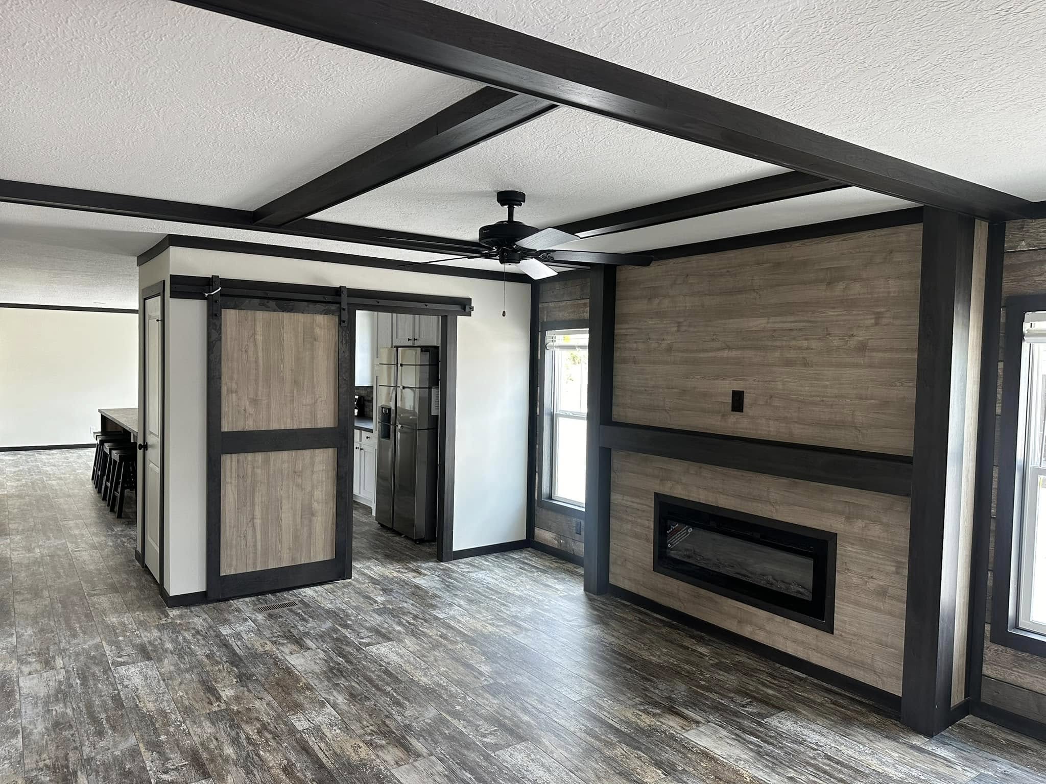 Open-concept living area with rustic wood accents, dark ceiling beams, and a modern electric fireplace. The space feels contemporary and spacious.