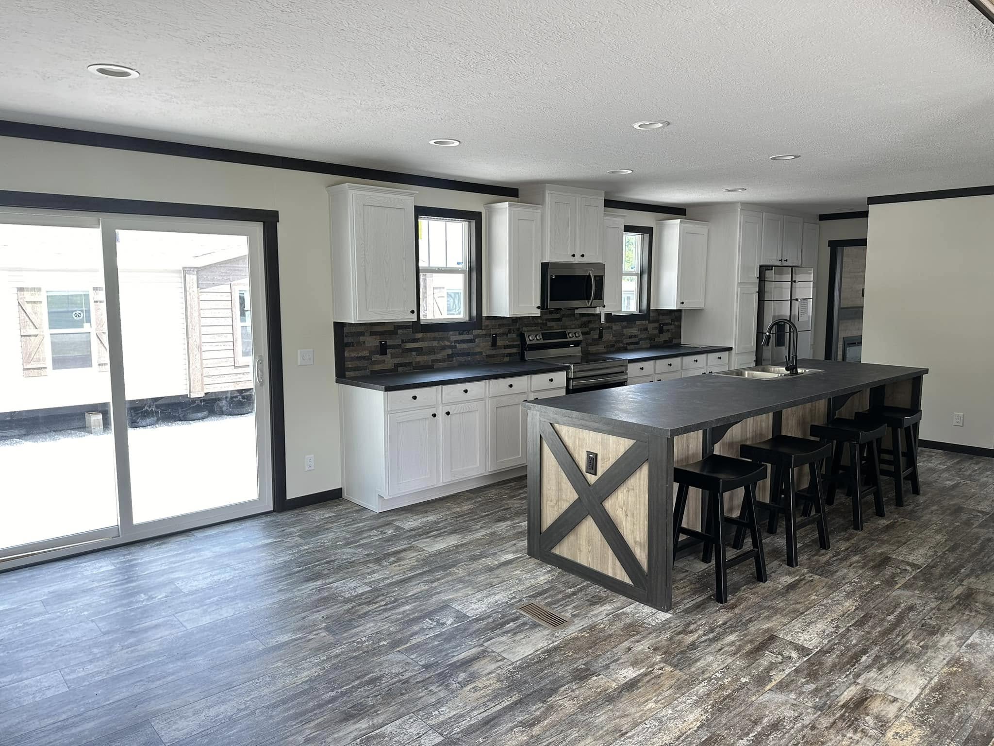 Modern kitchen with a rustic touch, featuring a large island with black stools, white cabinets, tiled backsplash, and sliding glass doors.