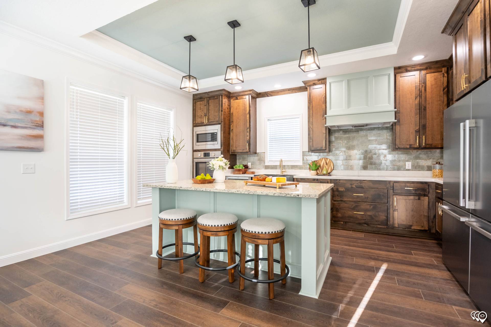 Bright, modern kitchen with wooden floors, dark wood cabinets, mint green island with granite countertop, and three cushioned stools. Sleek appliances and pendant lights enhance elegance.