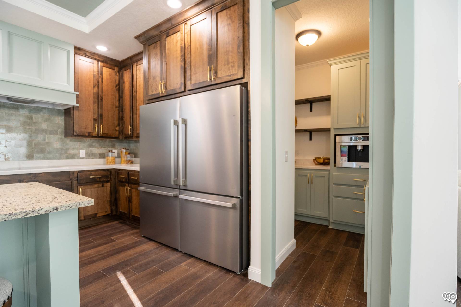 Modern kitchen with dark wooden cabinets, a stainless steel French door refrigerator, and green cabinetry. Warm lighting and wood floors enhance coziness.