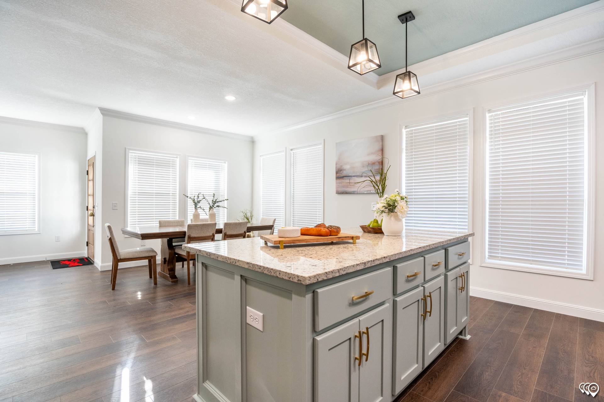 Modern kitchen and dining area with a large granite island, pendant lights, hardwood floors, and cozy décor. Bright and airy with natural light.