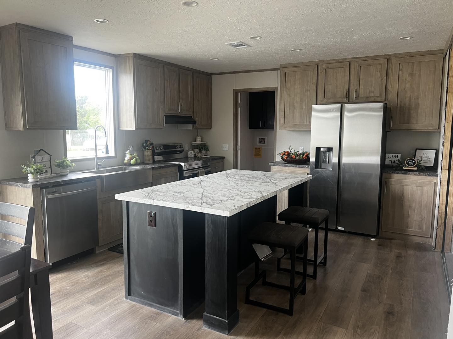 A modern kitchen with wooden cabinets, stainless steel appliances, and a marble-topped island with stools. Warm lighting creates a cozy atmosphere.
